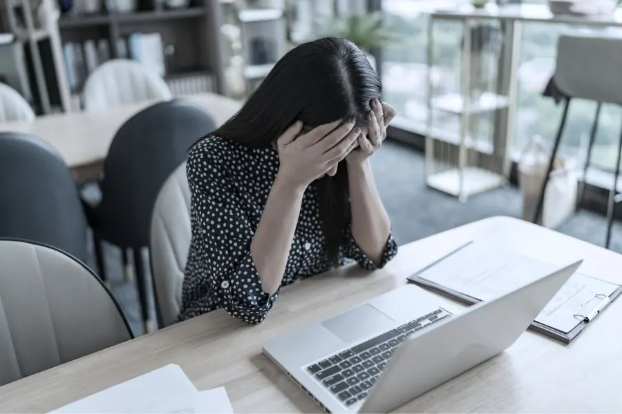 Femme assise devant son ordinateur, la tête entre les mains, illustrant la difficulté à gérer un client mécontent et la recherche de solutions pour apaiser la situation.