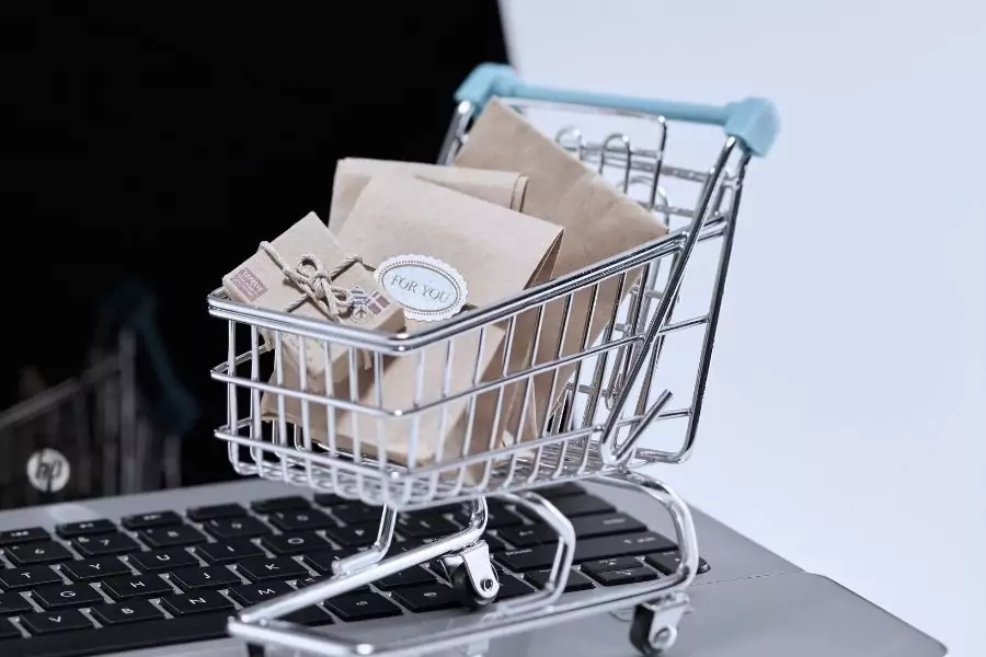 Chariot de courses miniature posé sur un clavier d'ordinateur portable, rempli de petits emballages, illustrant le droit de rétractation en e-commerce pour les créateurs et artisans d’art.